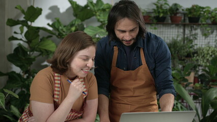 Naklejka premium Business partners at small flower shop discussing online orders using laptop computer
