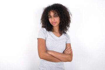Confident Young beautiful girl with afro hairstyle wearing grey t-shirt over white wall  with arms crossed looking to the camera