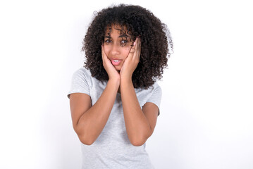 Fototapeta na wymiar Upset Young beautiful girl with afro hairstyle wearing grey t-shirt over white wall touching face with two hands