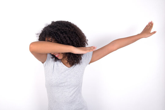 Photo of funky Young beautiful girl with afro hairstyle wearing grey t-shirt over white wall show disco move dab