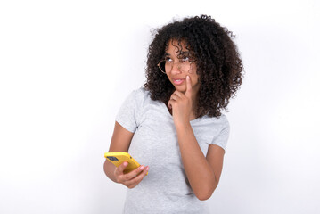 Young beautiful girl with afro hairstyle wearing gray t-shirt over white wall thinks deeply about...