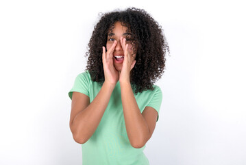 Fototapeta na wymiar Young beautiful girl with afro hairstyle wearing green t-shirt over white wall shouting excited to front.