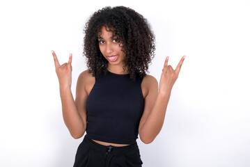 Young beautiful girl with afro hairstyle wearing black tank top over white background making rock...
