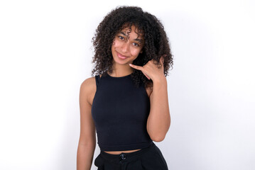 Young beautiful girl with afro hairstyle wearing black tank top over white background smiling doing phone gesture with hand and fingers like talking on the telephone. Communicating concepts.