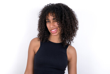 Young beautiful girl with afro hairstyle wearing black tank top over white background winking looking at the camera with sexy expression, cheerful and happy face.