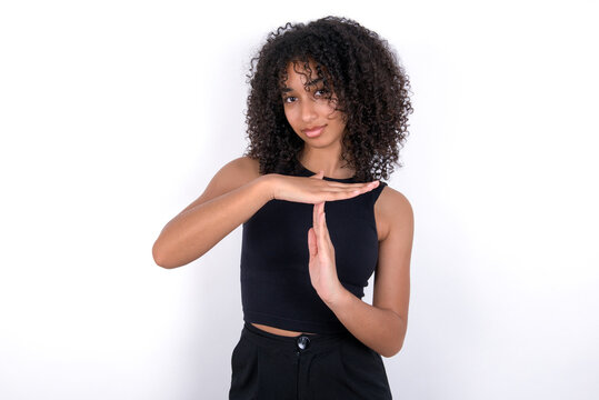 Young beautiful girl with afro hairstyle wearing black tank top over white backgroundbeing upset showing a timeout gesture, needs stop, asks time for rest after hard work, demonstrates break hand sign