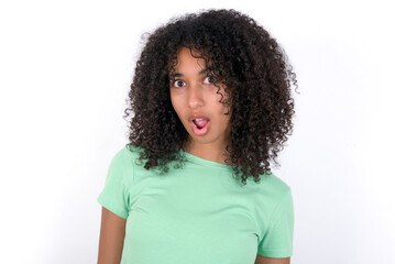 Fototapeta na wymiar Oh my God. Surprised Young beautiful girl with afro hairstyle wearing green t-shirt over white background stares at camera with shocked expression exclaims with unexpectedness,