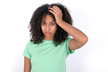 Embarrassed Young beautiful girl with afro hairstyle wearing green t-shirt over white background with shocked expression, expresses great amazement, Puzzled model poses indoor