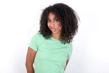 Fototapeta na wymiar Young beautiful girl with afro hairstyle wearing green t-shirt over white background keeps teeth clenched, frowns face in dissatisfaction, irritated because of much duties.