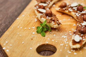Bananas with peanut butter, almonds and nuts, on wood plate on wooden board. Healthy food. Close up
