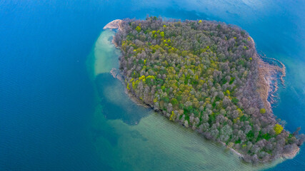 Top down view of the island in the shallow lake. Blue water and mixed trees.