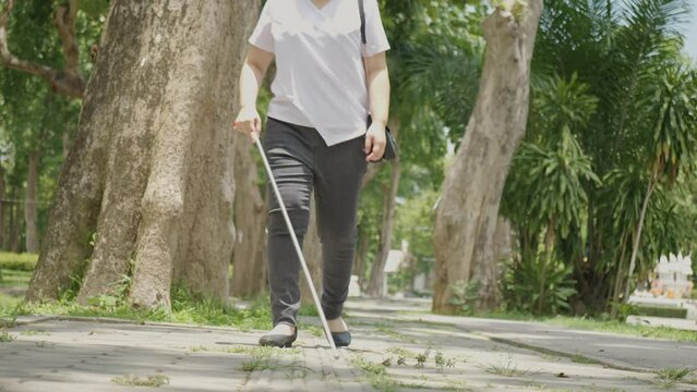 Asian woman with blindness disability walking on sidewalk contain tactile paving guide blocks using long white cane or blind cane a mobility tool to detect objects in the path for vision impairment 