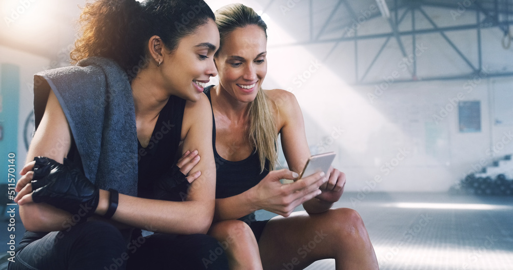 Poster Keeping up with the latest, anywhere, anytime. Cropped shot of two attractive sportswomen in the gym sitting down and reading text messages.