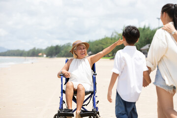disabled senior woman sitting in a wheelchair and family coming on the beach
