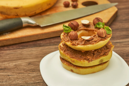 Apple rounds dialed on top of each other with peanut butter, almonds and nuts, on the table healthy food