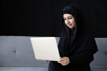 muslim woman using laptop computer on sofa and black background