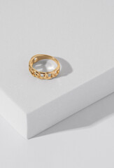 Vertical shot of chain shape golden ring on white podium with copy space