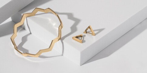 Panorama of Zig zag shape bracelet and triangle earrings on white podium with copy space