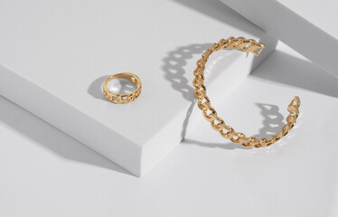 Chain shape golden modern bracelet and ring on white podium with copy space - obrazy, fototapety, plakaty