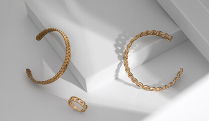 Shiny Modern gold braid shape and chain shape bracelets and ring on white geometric background