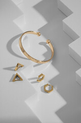 Top view of modern design golden bracelet and earrings on geometric white background