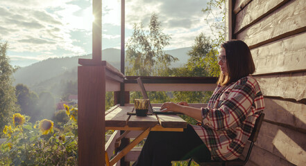 Woman working outdoor on terrace in sunny day in wooden cabin in the mountains of Ukraine