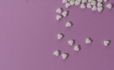 Top view of spilled heart shape white pills on purple background with copy space