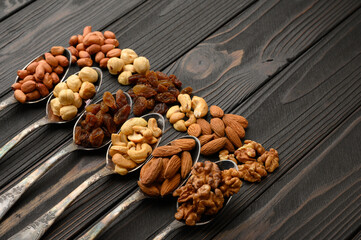 Hazelnut, cashews, raisins, almonds, peanuts, walnuts in silver spoons on a rustic background