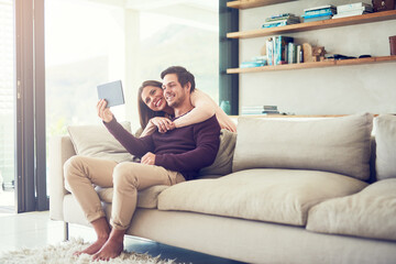 Obraz premium Wirelessly connected to friends and family. Shot of a smiling young couple using a digital tablet while relaxing on the sofa at home.