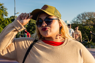 young latin woman outdoors at sunset, with cap glasses and looking at the camera giving a kiss