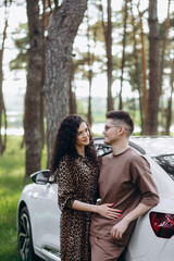 Near white colored car. Beautiful young couple have a good time in the forest at daytime.