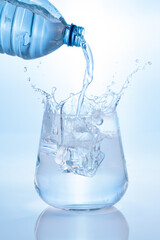 Pouring mineral water and splashing from bottle into glass on blue background. Vertical format.