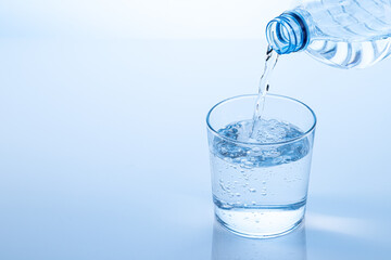 Pouring water from the bottle in to the glass isolated on blue background with copy space.