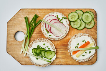 Rice cake with cream cheese and vegetables on wooden board