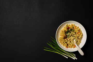 Instant noodles composition. Noodles and fresh vegetables and spices on bright black background