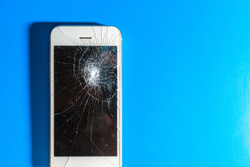 crashed smartphone with broken black screen on blue background. Top view. Repair concept.