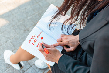 Woman writes in a notebook, holds felt-tip pen in her left hand.Outdoors summer evening park. Left-handers Day August 13th.Closeup.