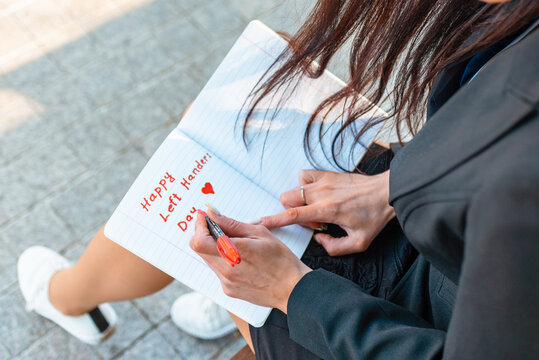 Woman writes in a notebook, holds felt-tip pen in her left hand.Outdoors summer evening park. Left-handers Day August 13th.Closeup. - Powered by Adobe