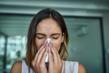 These allergies are the worst. Shot of a young businesswoman blowing her nose in an office.