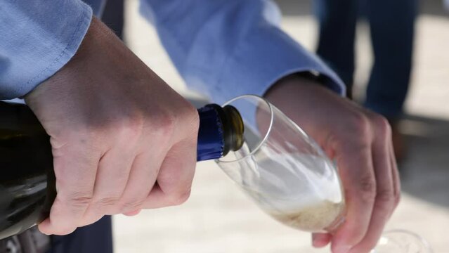 Close up of slowly pouring champagne from a bottle into a glass at a garden party or wedding party. Bubbles of champagne rising in the glass. 