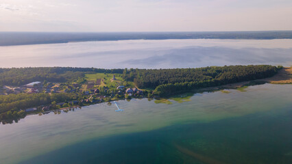 Aerial view of lake and small village on the peninsula. Sunset evening light by calm water on warm beautiful summer day.