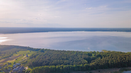 Obraz premium Aerial view of lake and small village on the peninsula. Sunset evening light by calm water on warm beautiful summer day.
