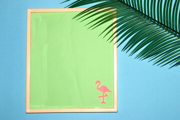 frame with pastel green background as copy space, on the background and pink flamingos, next to the frame flame leaf, creative summer design