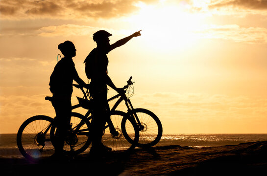Sunset exercise. Silhouette of a couple with their bicycles on the beach.
