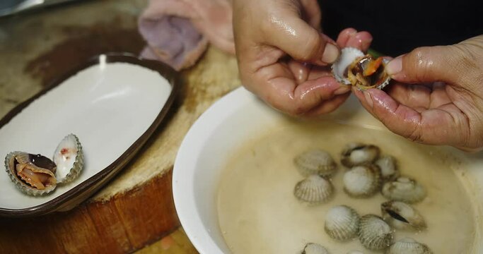 Close up person hand opens fresh juicy Steamed boiled cockle shell at the kitchen served with Thai style spicy sauce, Thai style seafood Thai food