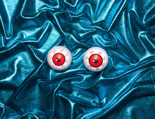 Funny eye balls on metallic blue creatively draped fabric background. Minimal horror layout.