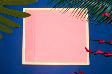 old retro frame with pink copy space on a blue background with palm leaves and flowers, creative...