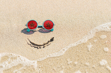 Obraz premium A painted smile on the beach and sunglasses with the flag of Morocco. The concept of a positive holiday in the resort of Morocco.