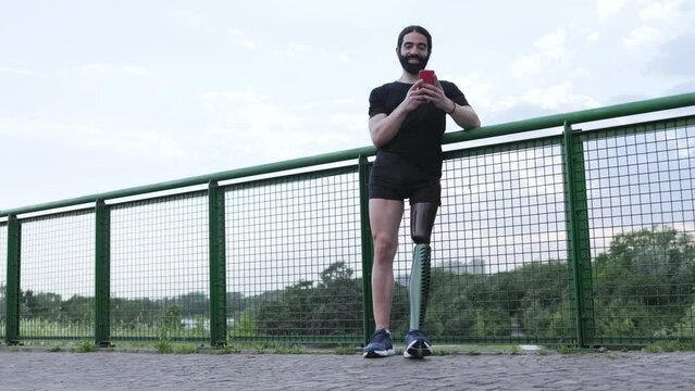 Young man with prosthesis leg using mobile phone outdoor at park city - Physical disability concept