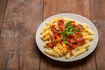 Beige plate with bolognese pasta on a wooden table sprinkled with green onions.